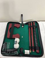 Mini putt set items displayed inside the open carrying case showing putter segments, golf balls, and the hole piece inside green felt lining.