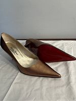 Side and bottom profile of one gold Laura Ferri high heel shoe showing the pointed toe, metallic gold leather upper, and red sole.