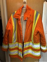 Front view of orange safety jacket hanging on a hanger showing reflective stripes and sherpa fleece lining inside.