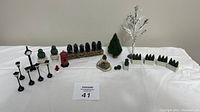 Complete set of miniature train set accessories arranged on white cloth showing all items in the lot including trees, lampposts, phone booth, clock, and small pond scene.