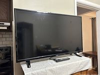 Front view of the flat screen RCA television on a white cloth-covered surface with remote control in front.