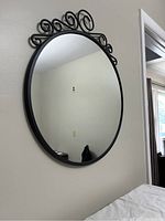 Front of round black metal framed mirror with curled metal decoration along the top