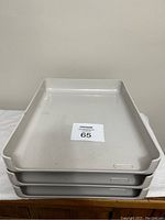 Three beige plastic trays stacked, showing top view with label '65'