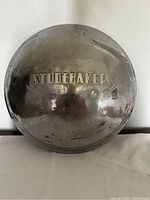 Front view of the Studebaker metal wheel hub cap showing embossed logo and surface wear.