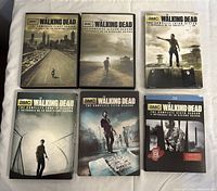 Front view of all six DVD box sets for The Walking Dead seasons 1-6 arranged in two rows of three. Each set displays distinctive cover art featuring characters in apocalyptic environments.