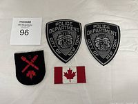 Photo of four patches including two NYPD black tactical police shield patches, one crossed torch and axe black patch, and one Canadian flag fabric patch.