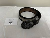Rolled-up black leather belt with visible eagle embroidery and oval metal buckle showing 'Red Man' and eagle with Native American chief design.