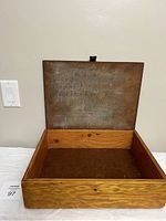 Open vintage wooden storage box showing interior and interior lid with faded inscription.