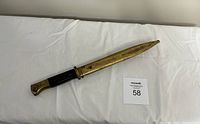 Full view of WW2 bayonet lying on white cloth with attached metal scabbard.