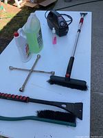 Photo showing windshield scrapers, brushes, Craftsman air pump, and cleaning fluids on a white table in daylight.