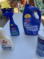 Four bottles/jugs of Bissell carpet cleaning supplies displayed on table outdoors