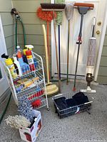 Metal trolley with various spray bottles and cans of cleaning products, gloves, cloth rags, brooms and mops, and a vintage vacuum cleaner.