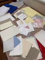 Various cross stitch fabric pieces laid out on a table showing different sizes, colors, and counts with some packaged pieces
