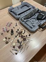 Dremel 8200 rotary tool accessories spread out on table including cutting discs, grinding stones, polishing wheels, sanding bands and mandrels in front of case.