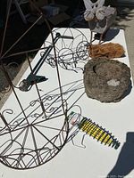 Overall assortment of garden decor items including metal wire plant holders, concrete planter, weathered metal owl and coir piece on white table outdoors