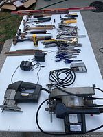 Full lot view showing hand tools, power tools, and measuring tools spread on a table outdoors.