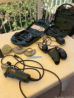 Complete lot showing two Metabo cordless hand screwdrivers, metal corded electric grinder with power cord, two extra batteries, charger, sanding disc, sanding pad, and wrench in a plastic case and accessories on a white table.