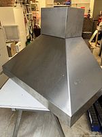 Front angle view of the stainless steel range hood showing its pyramid shape and metallic finish.