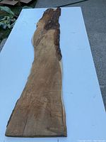Full view of the raw edge wood board placed on white surface showing natural bark along one edge and smooth sanded surface on the opposite side.