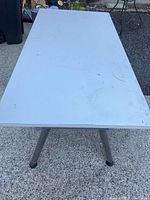 Top down photo showing rectangular white work table surface with visible wear and marks.