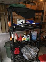 Full view of black plastic shelving unit with automotive fluids and accessories including antifreeze, motor oil, funnel, squeegee, snow brush, tarps, mats, and trash bags.