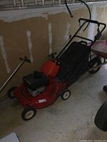 Full side view of red MTD gas lawn mower with handle folded against wall