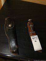 Two hunting cutters with their sheaths on a dark surface, one sheath black leather, the other brown leather.