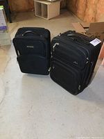Two black carry-on size suitcases, approx 20 and 21 inches tall, positioned on a concrete floor.
