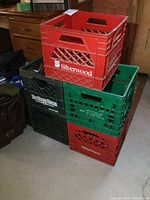 Five plastic milk crates stacked, including red Silverwood and green Heritage Farm crates, showing brand logos and crate design.