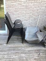 Stack of six patio chairs and folded protective cover on wooden deck.