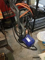 Full view of Simoniz blue electric pressure washer unit with hoses and extension cord coiled on handle.