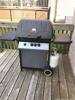 Full view of the Sterling propane BBQ grill on a wooden deck, showing the black grill with side shelves and propane tank attached.