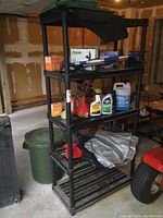 Full view of black resin shelf in garage with various items on shelves and some dust visible