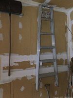 Full view of aluminum step ladder standing against drywall with visible wall patching and ceiling corner.