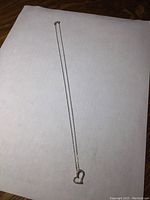 Full view of the 18 inch sterling silver chain necklace with heart pendant laid flat on white surface.