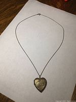Full view of heart-shaped locket pendant on chain laid flat