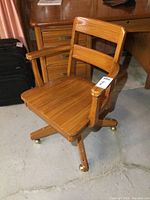 Front view of vintage solid wood office chair with seat, armrests, and casters on legs.