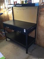 Front view showing overall workbench with pegboard back, two drawers, lower shelf, overhead light