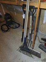 Photo of the collection of yard tools leaning against a wall: rake, fork, shovel, hoes, broom, weed puller