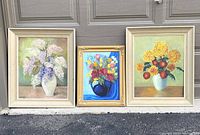 Three floral still life oil paintings displayed side by side, showing varied frame and size styles. Two large paintings with lilacs and one smaller multicolored floral painting.