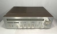 Front view of AKAI AA-1040 stereo receiver showing the frequency display, control knobs, and switches on silver metal panel with wooden top enclosure