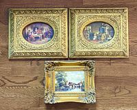 Three oil paintings displayed together on wooden floor, shows ornate gold gilt frames and detailed scenes in oval and square paintings.