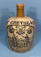 Front view of tan ironstone whiskey bottle with 'The Greybeard' text and illustrated Scottish figures.