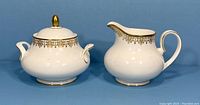 Photo showing front view of white Royal Doulton creamer jug and sugar bowl with gold lace decoration, lid on sugar bowl with gold finial.
