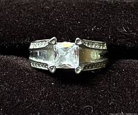 Front view showing the clear square-cut center stone and side accent stones on split shoulders of sterling silver ring.