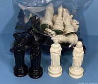 Black and white Renaissance style chess pieces arranged in front of a plastic bag with more pieces inside, showing different figures and details.