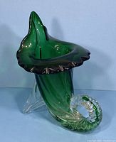 Front angle showing the green art glass cornucopia vase with ruffled lip and clear glass tail base.