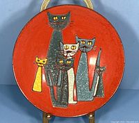 Front view of the round enameled dish on stand showing full cat design and red background