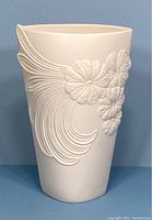 Front view of white bisque vase featuring raised floral and flowing abstract design on front side.