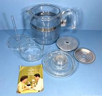 All disassembled components of the Pyrex coffee percolator laid out including glass parts, metal filter plates, and original booklet.